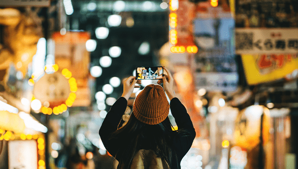 Vrouw maakt een foto met haar smartphone in een kleurrijke, verlichte winkelstraat